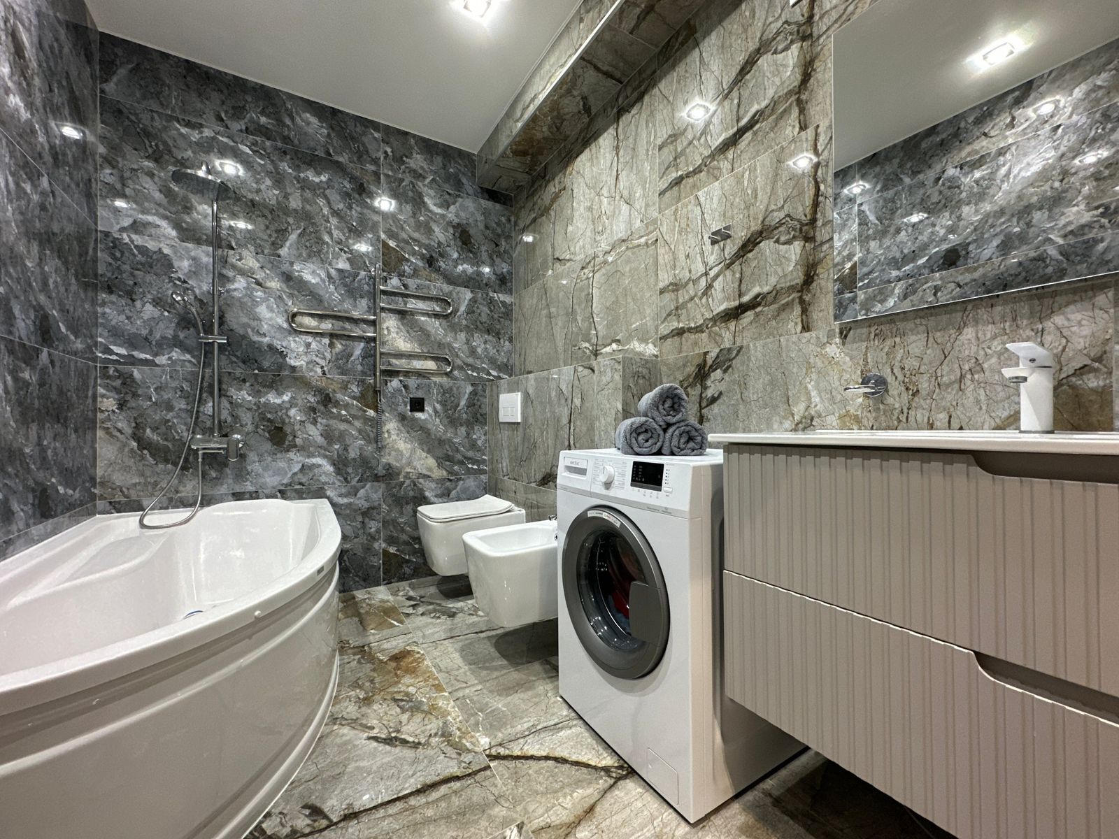 Marble-tiled bathroom with corner bath, shower, washing machine and vanity