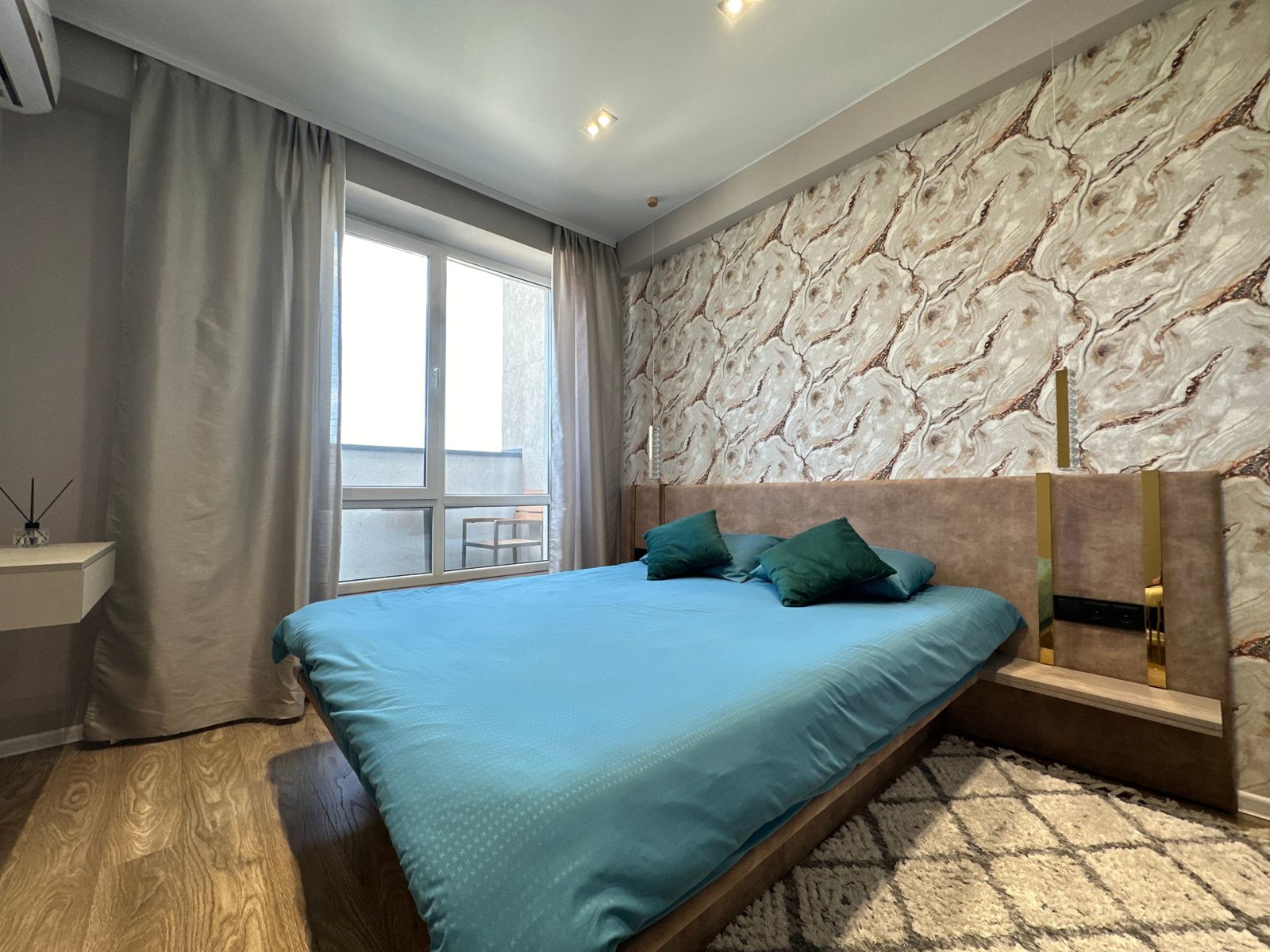 Bedroom with a large bed in teal linen, marble-pattern wall and a balcony window