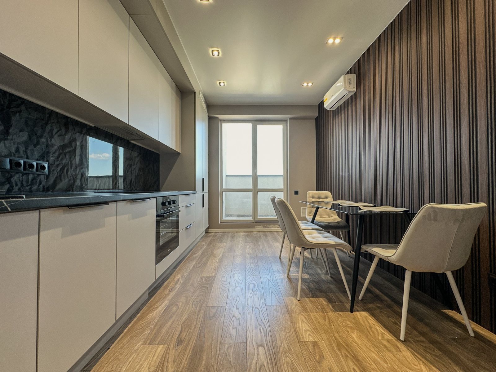 Long kitchen with oven and a glass dining table with four chairs