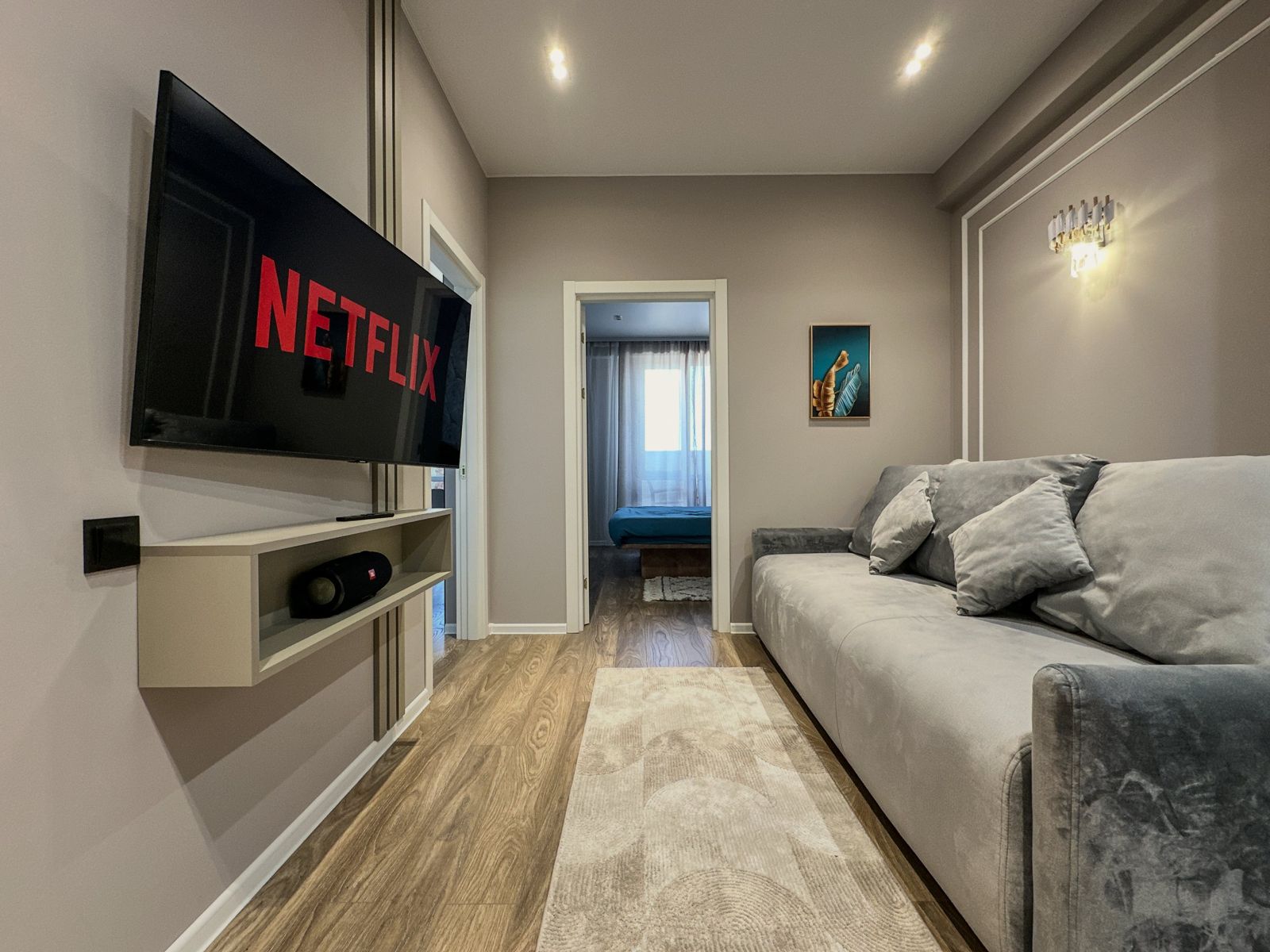 Living room with grey sofa, wall-mounted TV and the bedroom door beyond